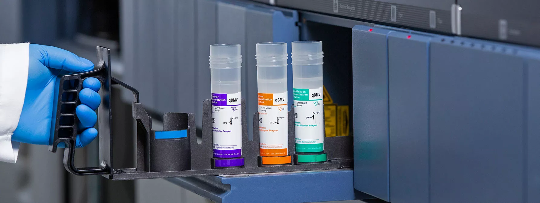 gloved hand putting test tubes into lab equipment