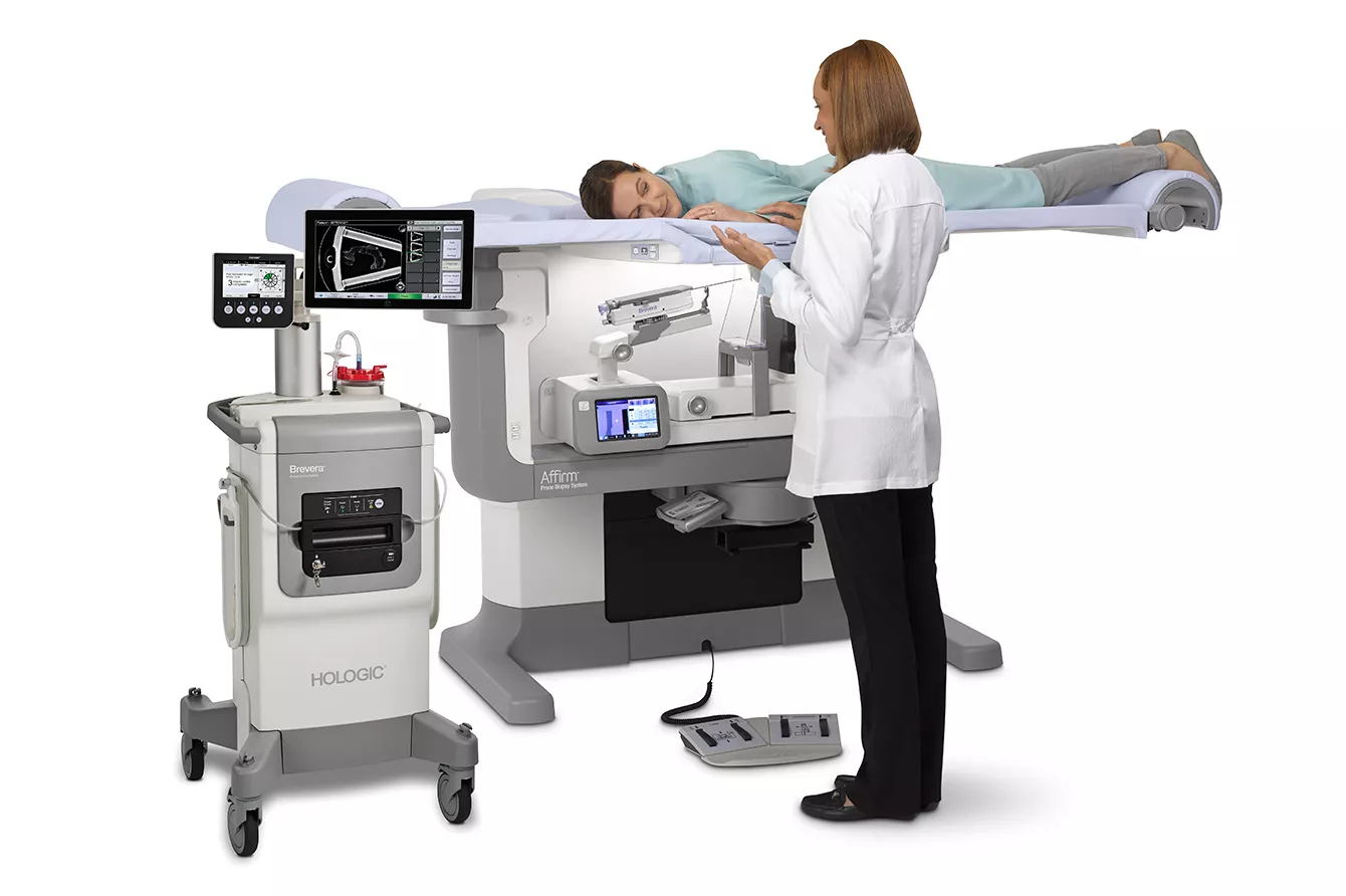 Profissional de saúde ao lado da paciente deitada no sistema de biopsia mamária